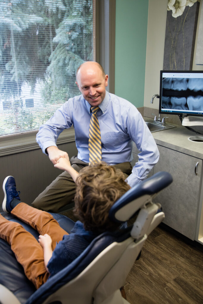 Dr. Scott J. Shumway DDS, smiling and talking to a young patient in the clinic